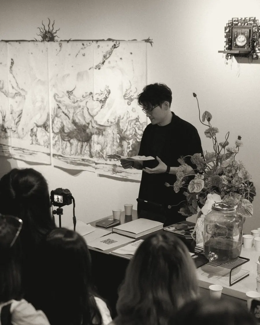 A speaker at a table with flowers and books, facing guests