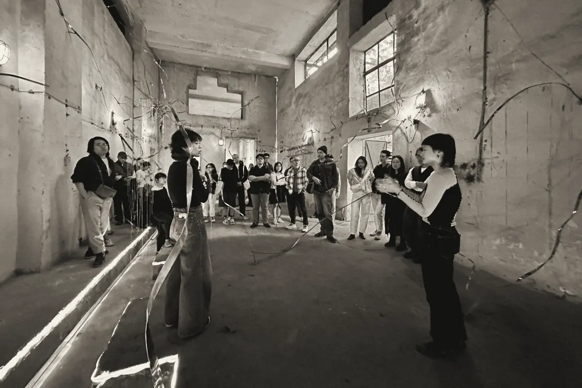 An audience among metal ribbons strung across an old factory room