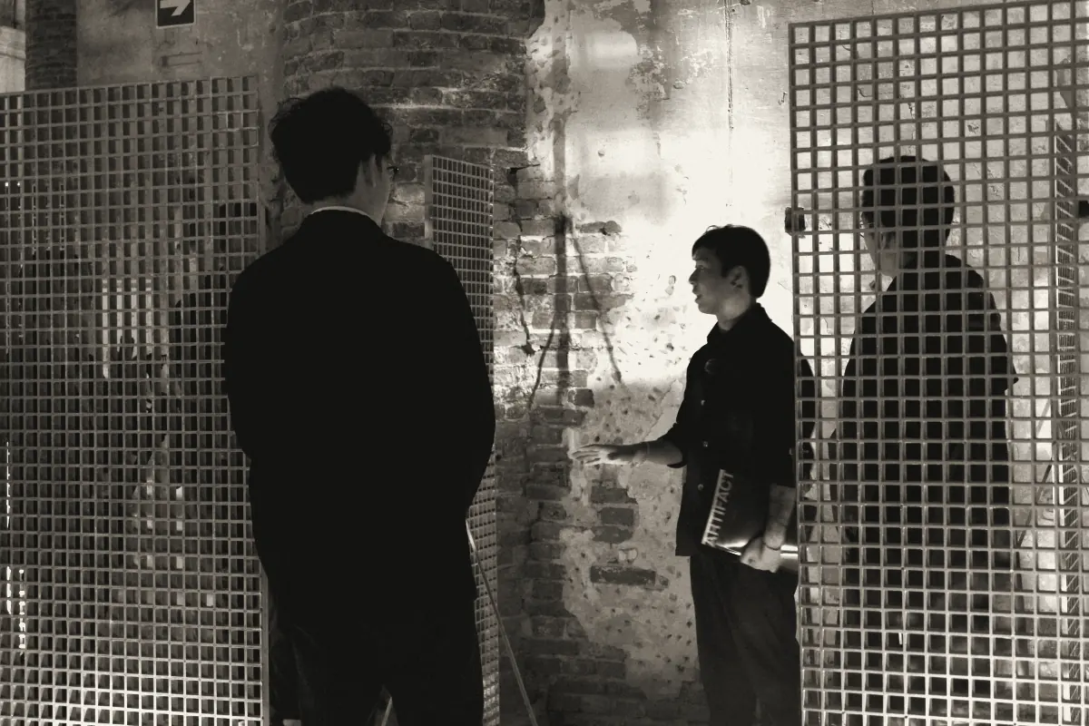 A walkthrough among steel grid panels in Venice, the guide holding a copy of the Journal