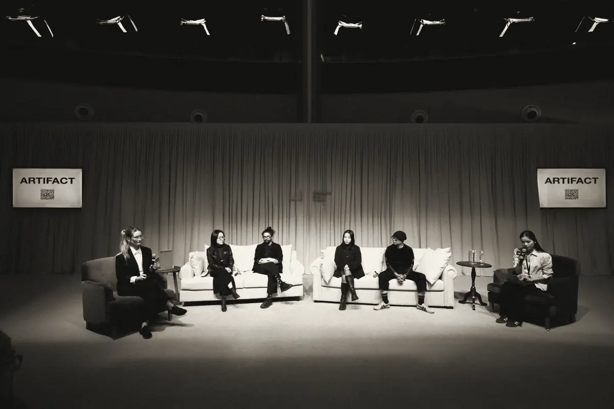 Six speakers on a stage under two ARTIFACT screens